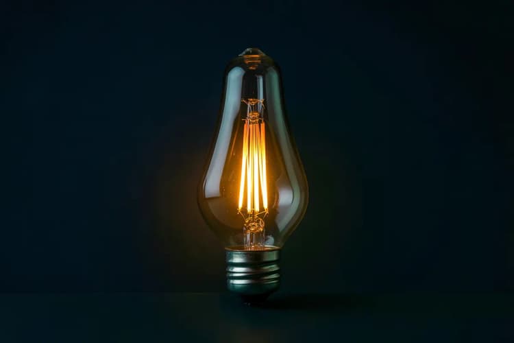 Um conjunto de três lâmpadas incandescentes acesas, com uma delas brilhando mais intensamente, simbolizando ideias e destaque.